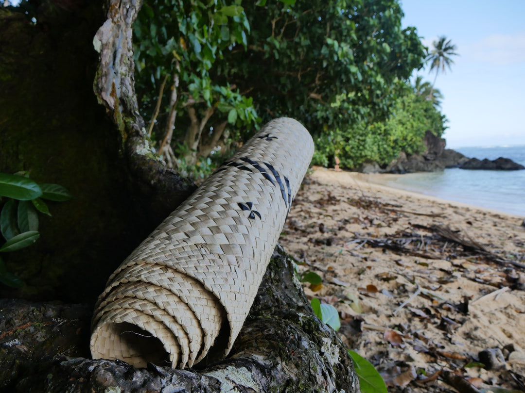 Pandanus plant woven yoga mat resting against a tree truck on a Fijian beach - Tali Tali | Eco Yoga Store