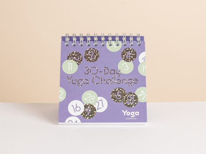A spiral-bound '30-Day Yoga Challenge' by Yoga Journaling, featuring a purple cover decorated with light green and white numbered circles and glittery gold numbers, set against a neutral beige background - Yoga Journaling | Eco Yoga Store