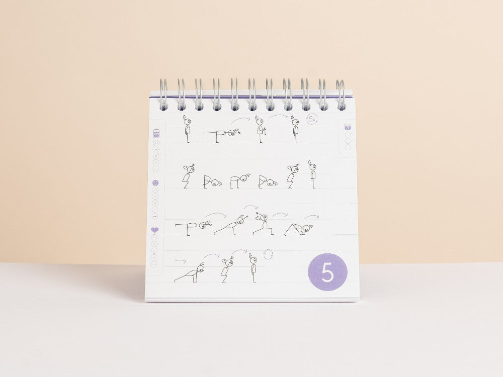 A spiral-bound'30-Day Yoga Challenge' standing upright on a white surface against a warm beige background. The page features small line-drawing diagrams arranged in rows and a purple circle near the bottom containing the day sequence, number 5 - Yoga Journaling | Eco Yoga Store