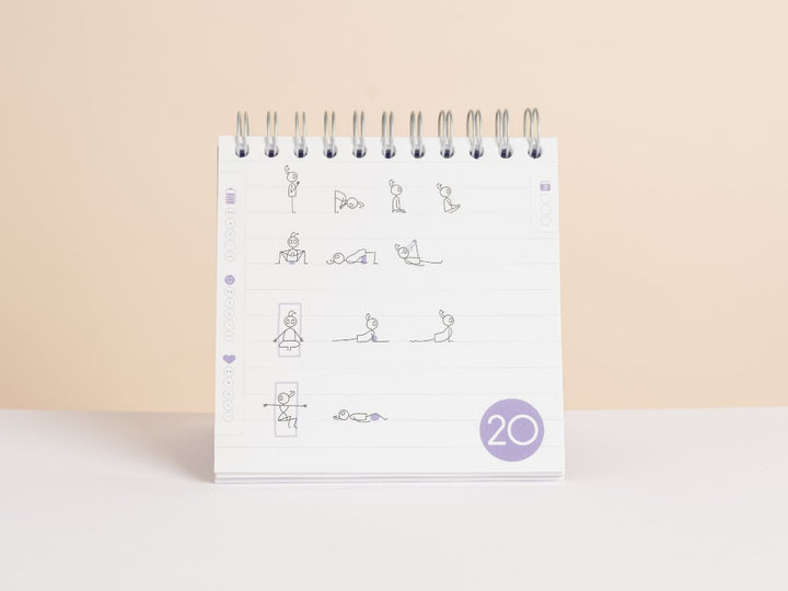 A spiral-bound '30-Day Yoga Challenge' standing upright on a white surface against a warm beige background. The white page features simple black line-art illustrations of yoga poses, with a purple day sequence circle at the bottom right labeled '20' - Yoga Journaling | Eco Yoga Store