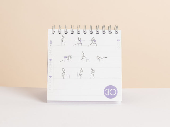 A spiral-bound '30-Day Yoga Challenge' standing upright on a white surface against a warm beige background. The white page features simple line drawings of people performing exercises and a purple day sequence circle near the bottom with the number 30 - Yoga Journaling | Eco Yoga Store