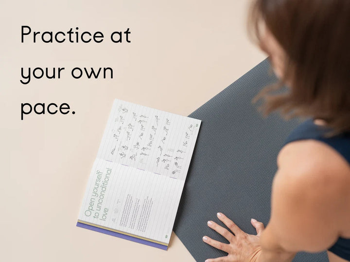A woman, seen from behind, placing her hand on a Manduka PROLite yoga mat next to an open Chakra Flow book. The background is a solid light beige wall with the text 'Practice at your own pace - Yoga Journaling | Eco Yoga Store