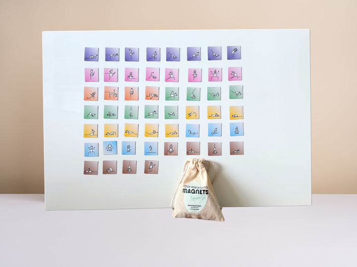 A white magnetic alignment board with 36 Yoga Sequencing Magnets (Expansion Set) in a grid, shown standing upright on a light surface against a beige wall. A drawstring storage pouch sits in front of the board - Yoga Journaling | Eco Yoga Store