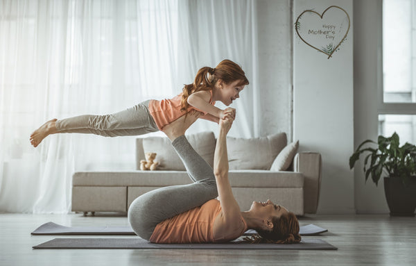 Mother lying on her back supporting her young daughter above her with her feet | Eco Yoga Store