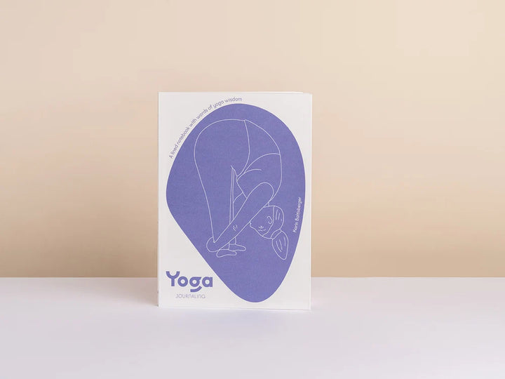 Yoga Journaling Notebook standing upright on a white surface against a warm beige background. The cover features a large lavender-purple abstract shape containing a minimalist line drawing of a person in a yoga pose - Yoga Journaling | Eco Yoga Store